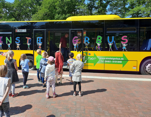 Bild vergrößern: Schulkinder beim Einstieg in einen bunten Autobus mit dem Schriftzug "Einsteigerbus".